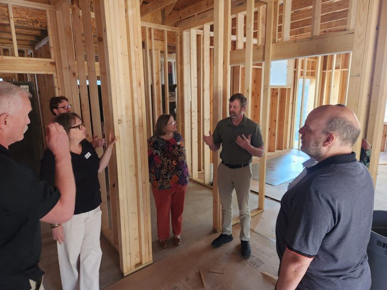 A group tours a building under construction, its wood framing still open