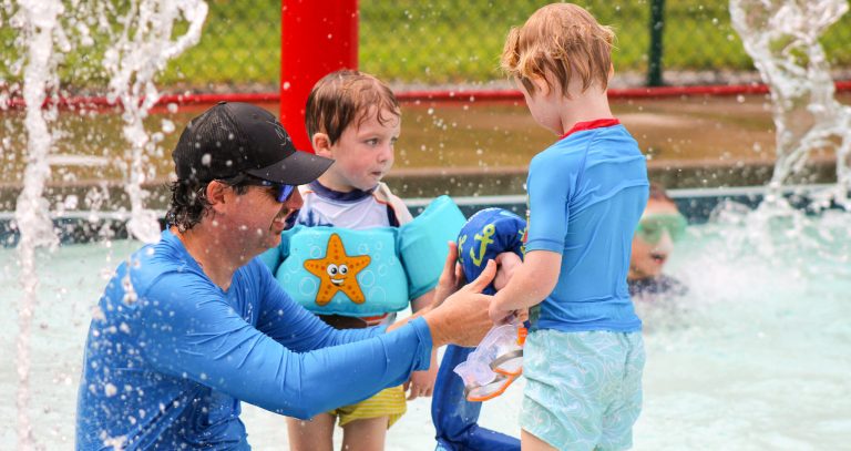 An adult helps two young children in swim gear at the Lutheridge splash pad