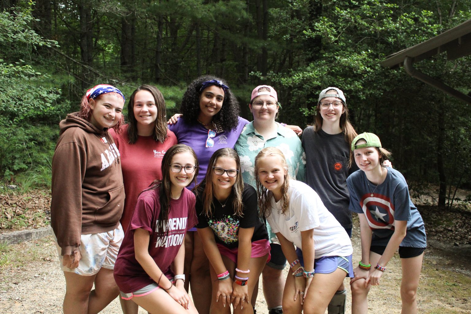 A youth group of smiling teenagers huddled together in the woods at camp