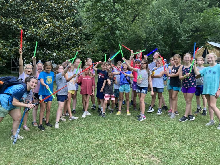 Campers in a grassy field at Lutheridge raise colorful glow sticks over their heads with their counselor