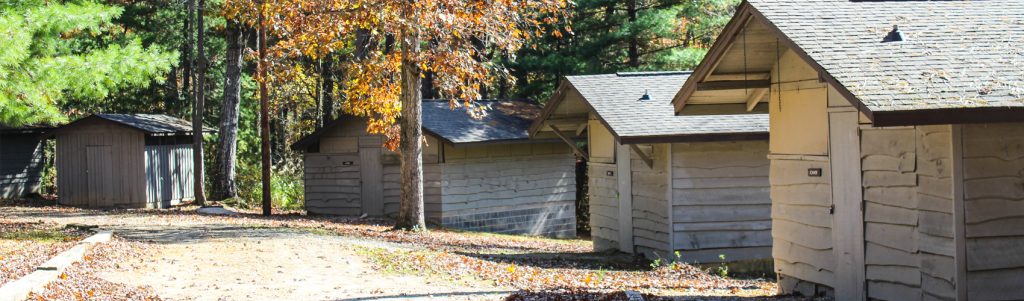 A row of Pioneer Cabins, small gray camp cabins among fall trees