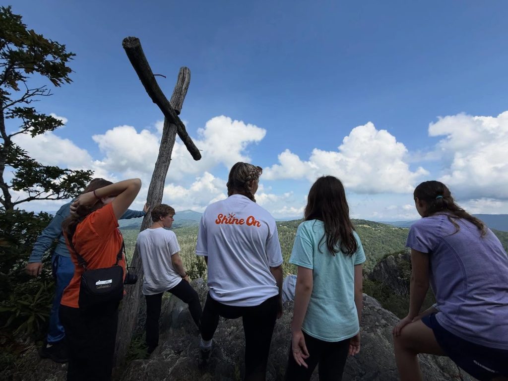 Campers on the rock beside the wooden cross at Lutherock, looking out over the mountains