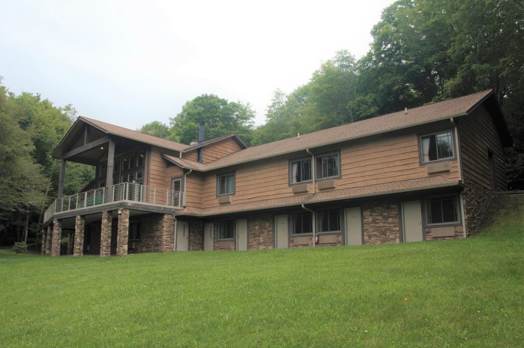 Crow’s Nest at Lutherock, a two-story wood lodge with a balcony on stone pillars above a sloping lawn