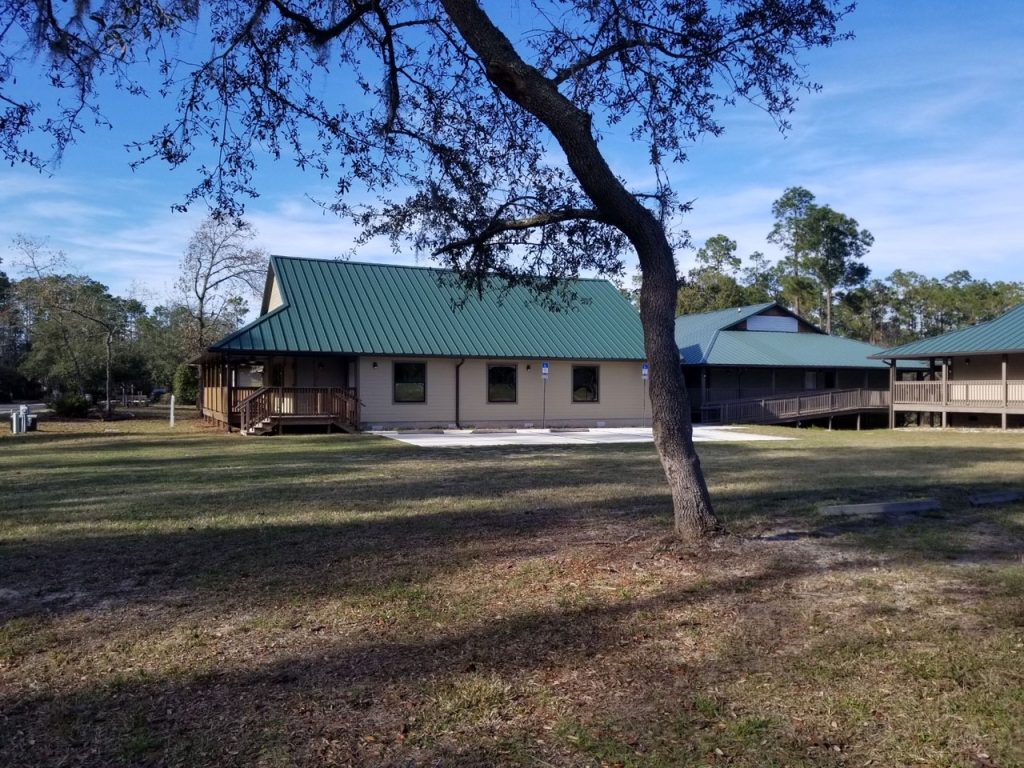 Atonement Chapel at Luther Springs, a tan building with a green metal roof, seen past an oak tree
