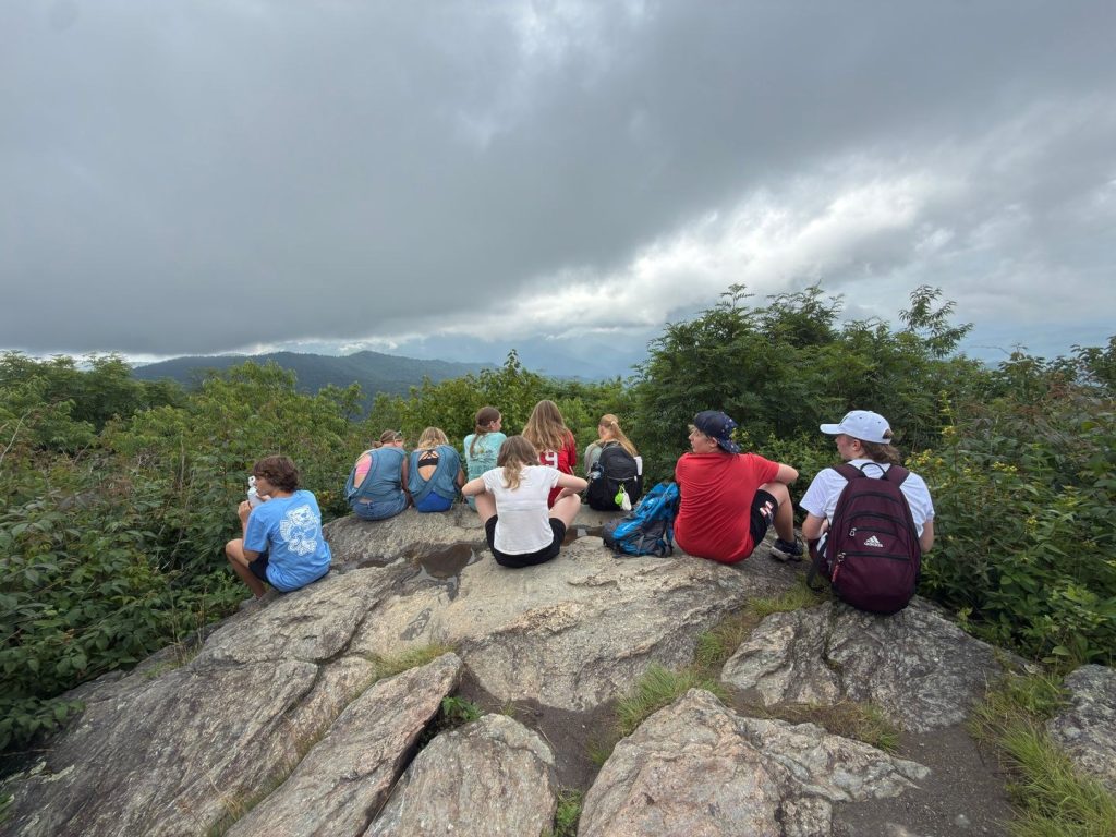 Teen campers sitting together on a rock outcrop above the mountains