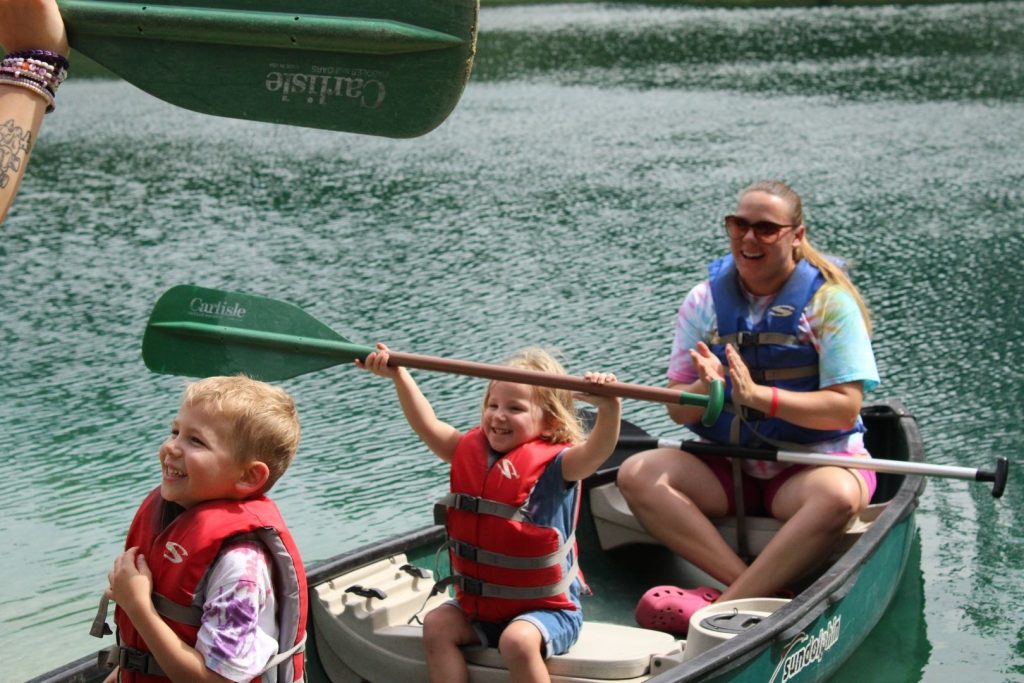 A family in a canoe on the Lutheridge lake raising their paddles at bRIDGE Family Camp