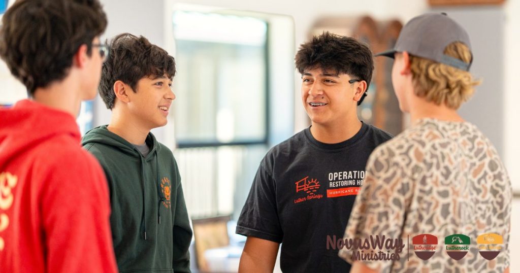 Four teenage campers talk and laugh together, one in a Luther Springs Operation Restoring Hope T-shirt