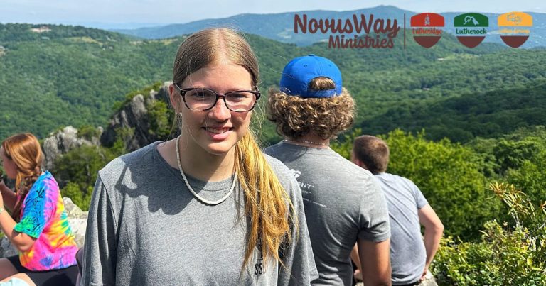 A smiling camper at a mountain overlook above forested ridges, other campers beside her