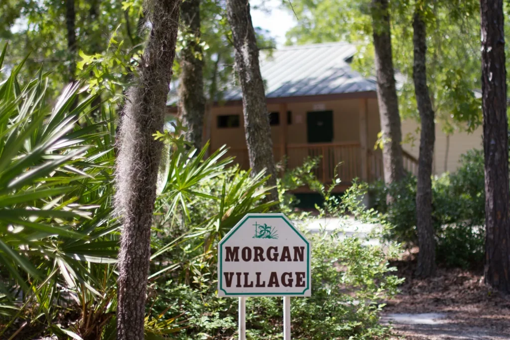 The Morgan Village sign among palmettos and pines at Luther Springs, a cabin in the trees behind it