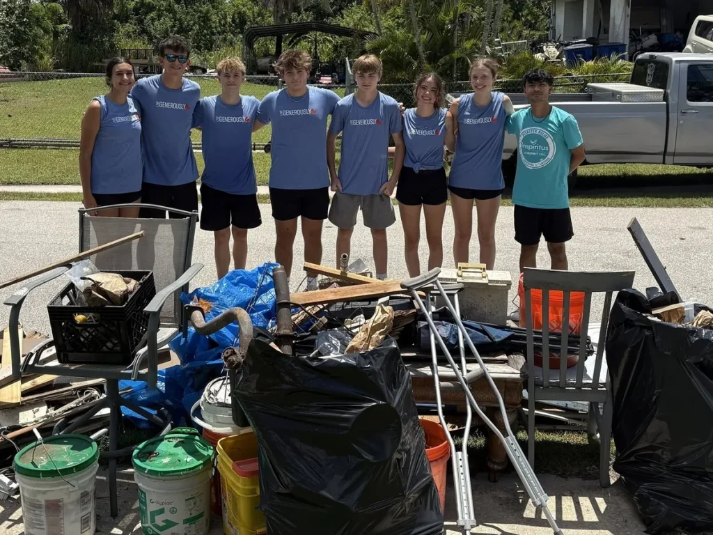 A youth team in matching shirts standing behind a pile of storm debris they cleared on a Luther Springs disaster response trip