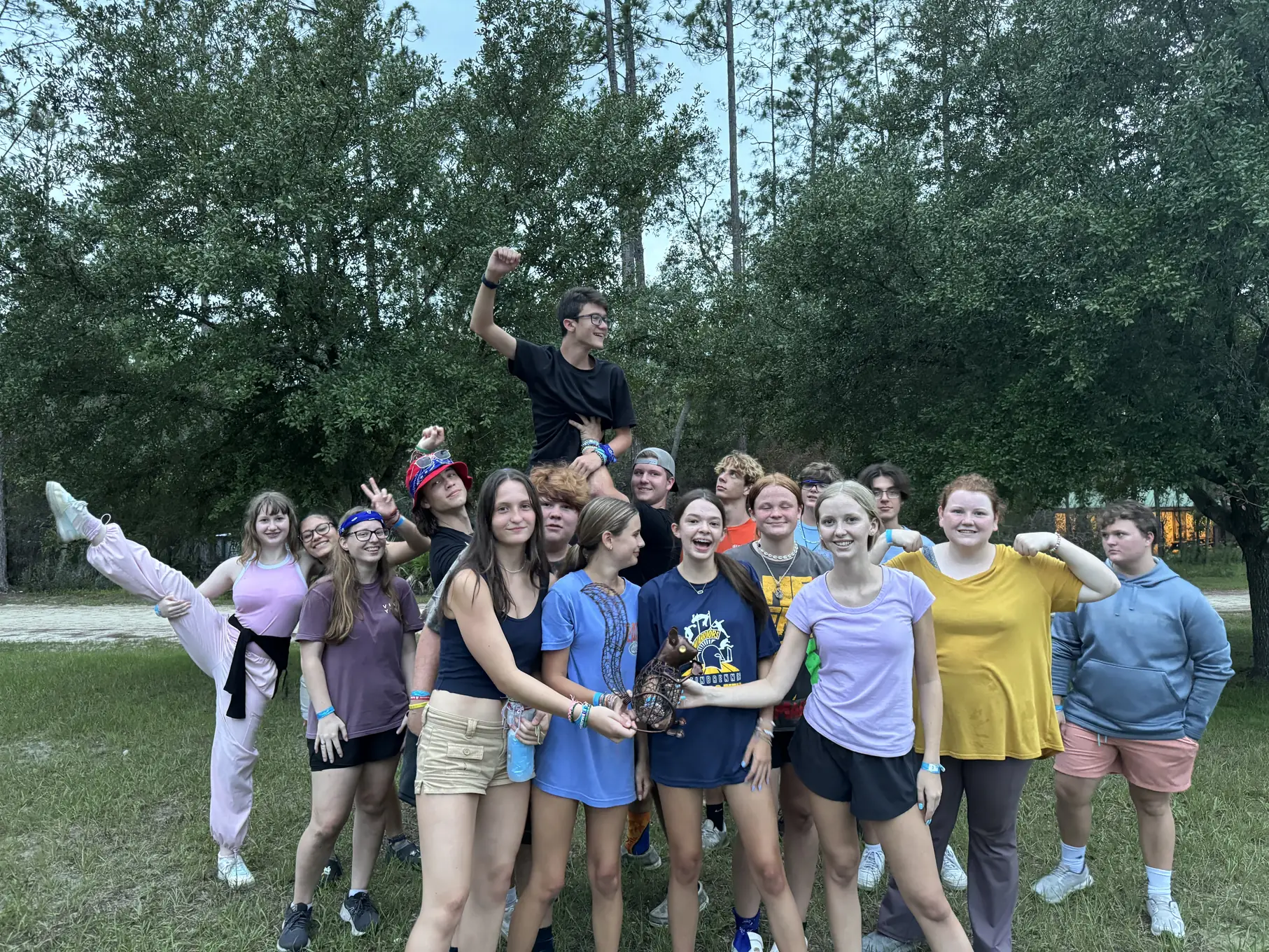 Teen campers cheer together outdoors for a group photo during Gators week at Luther Springs