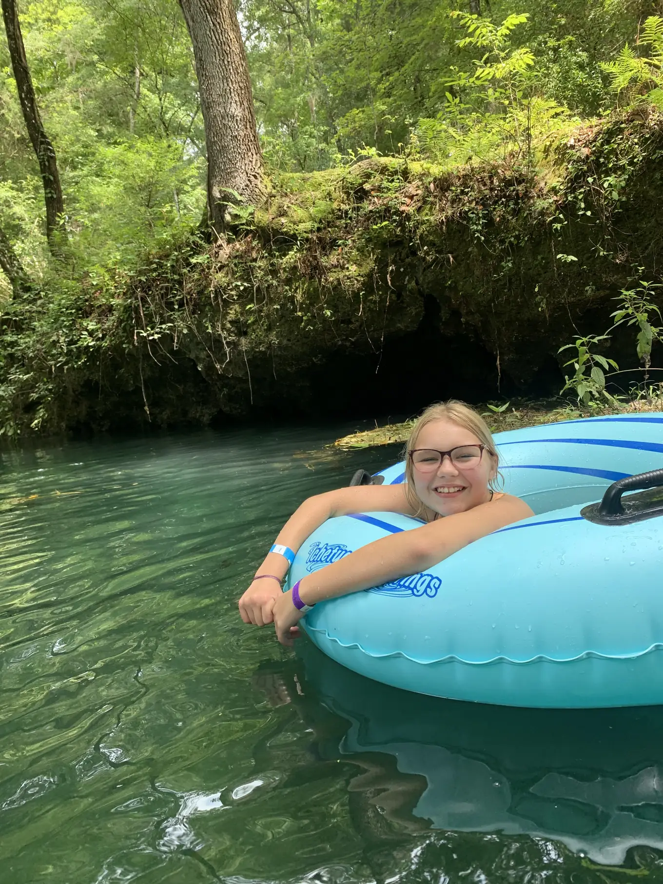 A smiling camper floats in a blue tube on a clear spring river