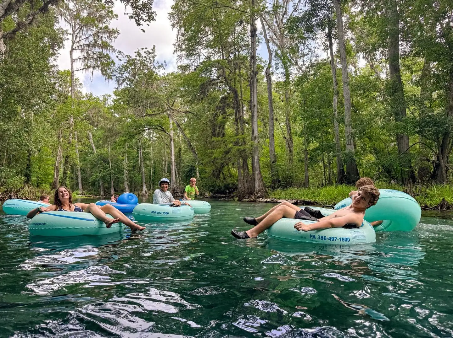 Campers float in tubes down a clear, tree-lined spring run
