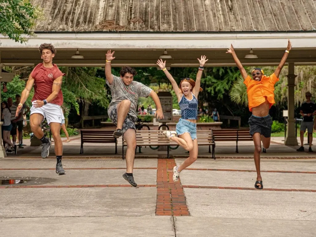 Four Luther Springs summer staff jumping in the air on the brick walk in front of the pavilion