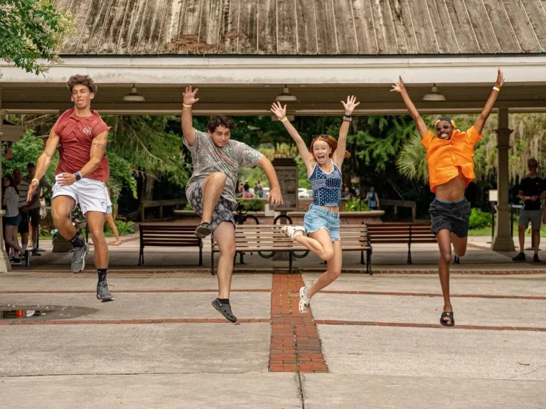 Four Luther Springs summer staff jumping in the air on the brick walk in front of the pavilion
