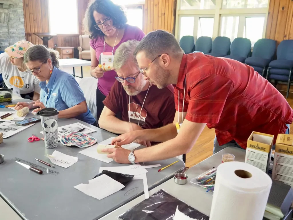 Retreat guests at a long worktable of tools and tissue paper, one leaning in to help another
