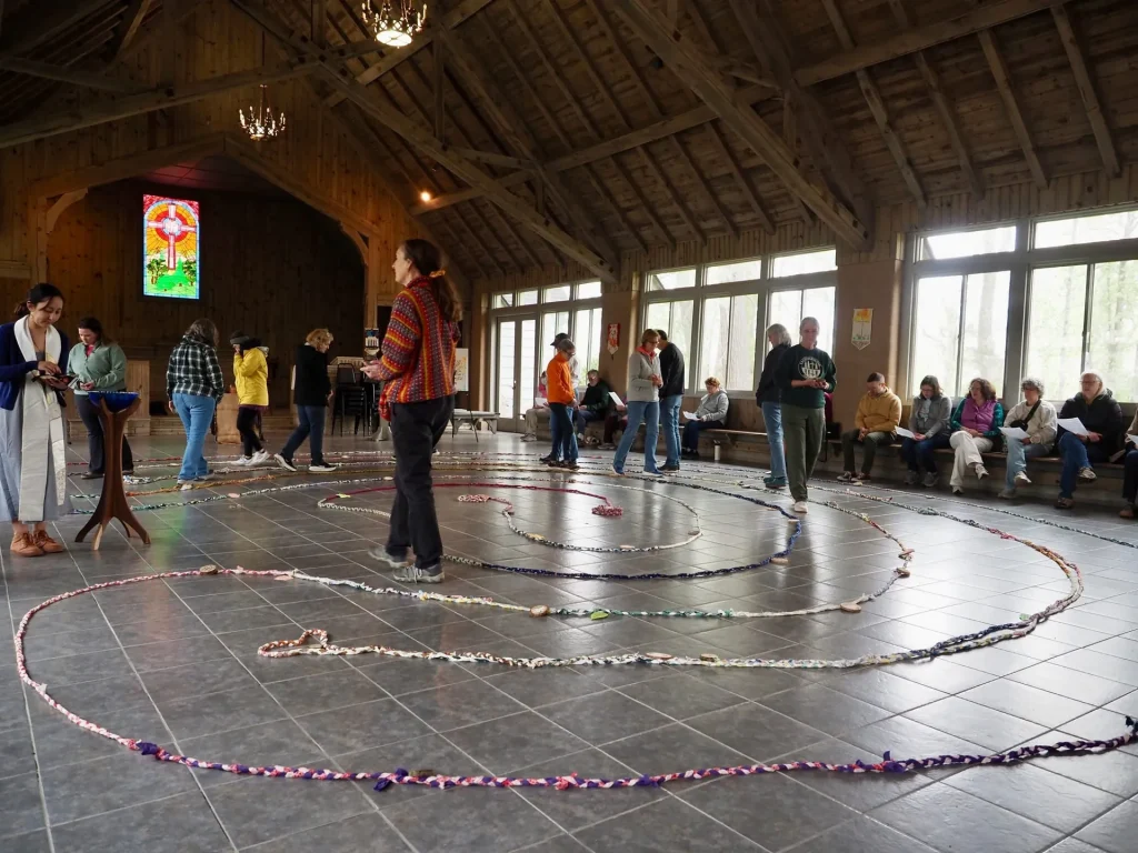 Guests walk a labyrinth of braided cloth laid on the floor of a timber hall with a stained-glass cross window