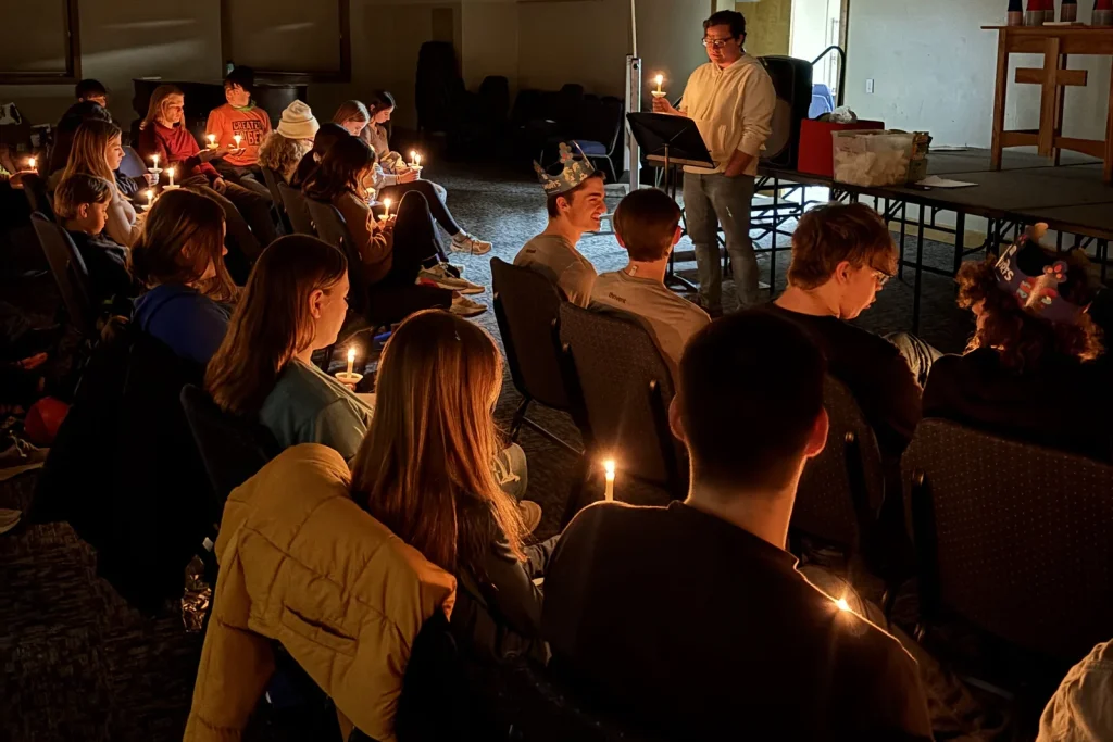 Youth holding lit candles during evening worship at Faith Ablaze, a leader standing at the front with a candle