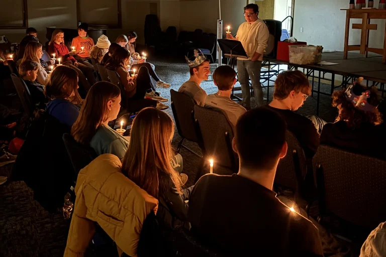 Youth holding lit candles during evening worship at Faith Ablaze, a leader standing at the front with a candle