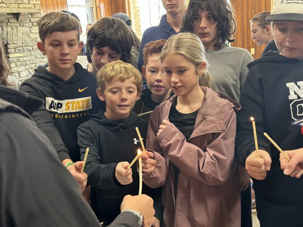 Youth light thin taper candles from one another during worship
