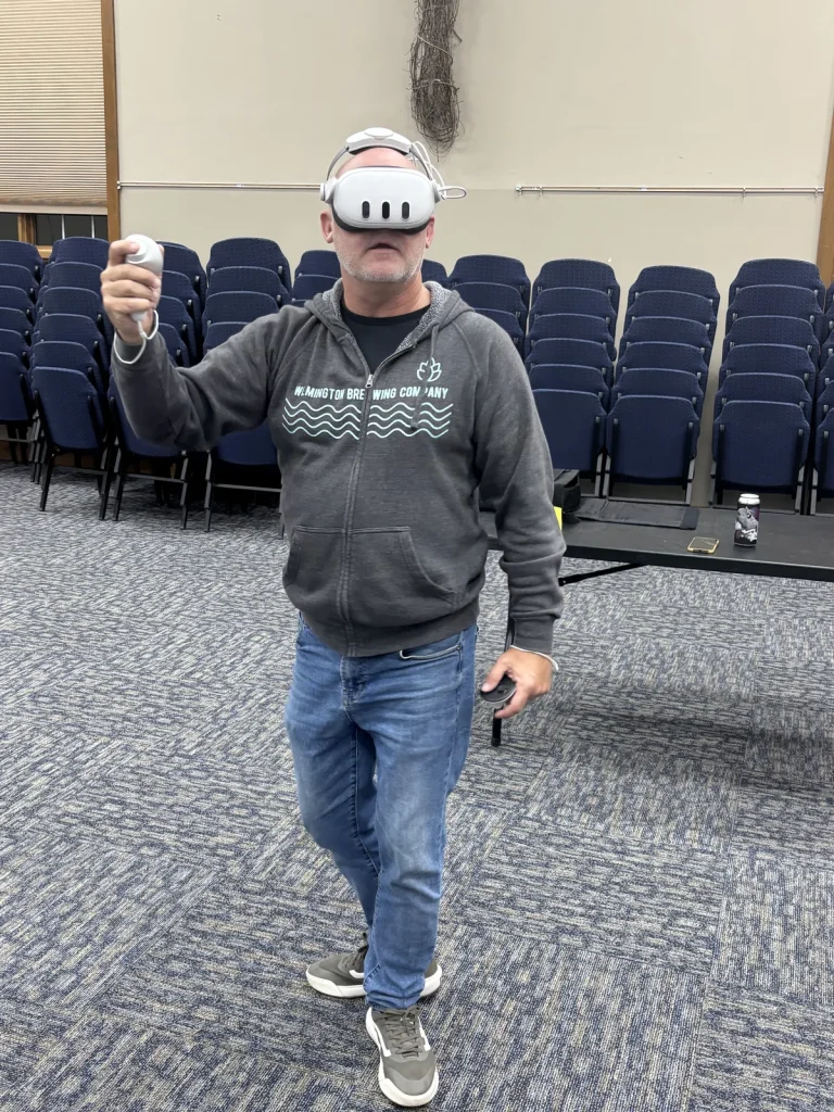 A guest in a virtual reality headset raising a controller in the middle of a meeting hall