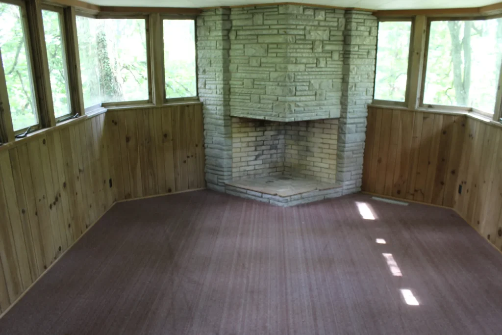 A Mission Hall room with a stone corner fireplace and windows