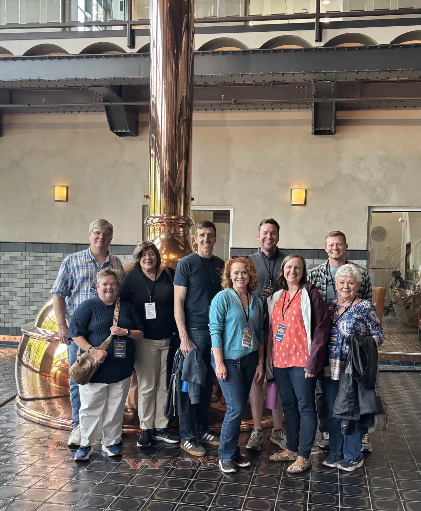 A Theology On Tap group beside a copper brew kettle on a brewery tour