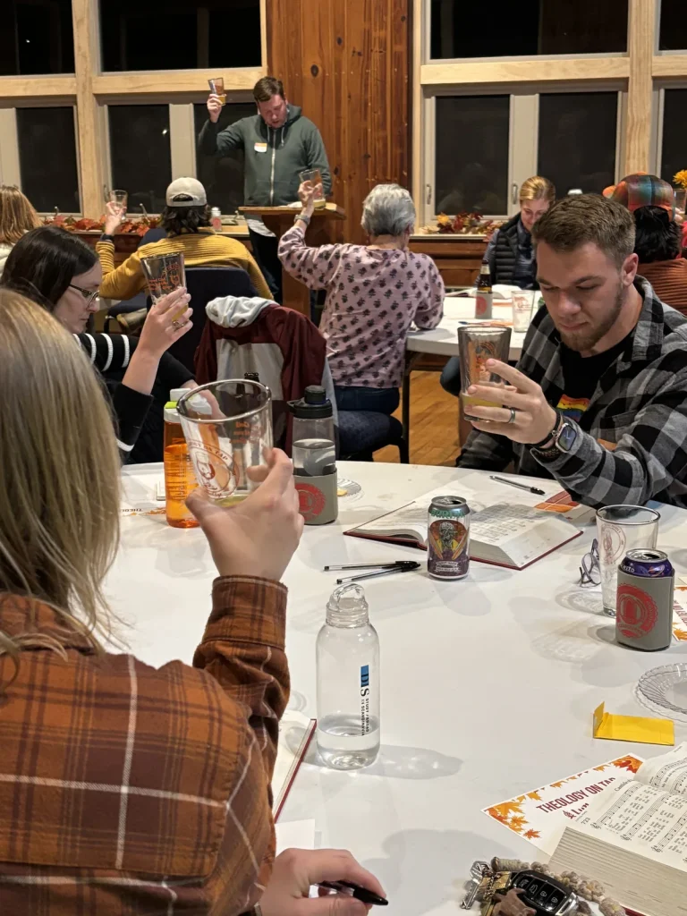 Guests raising tasting glasses during an evening Bible study, an open Bible on the table