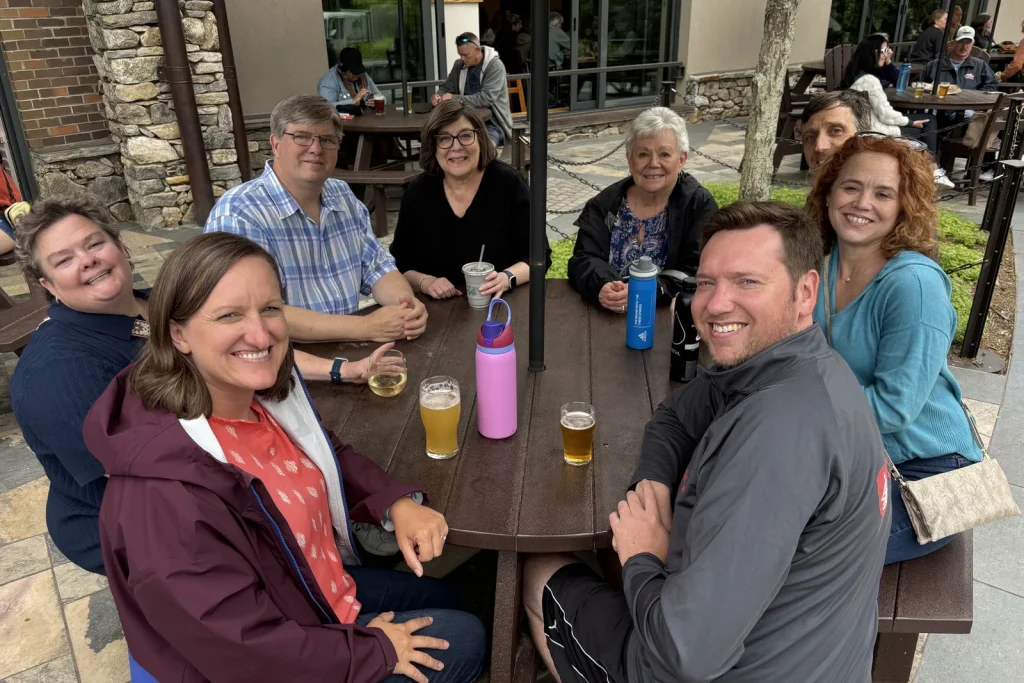 Theology On Tap friends smiling around an outdoor table at a brewery, glasses of craft beer in front of them