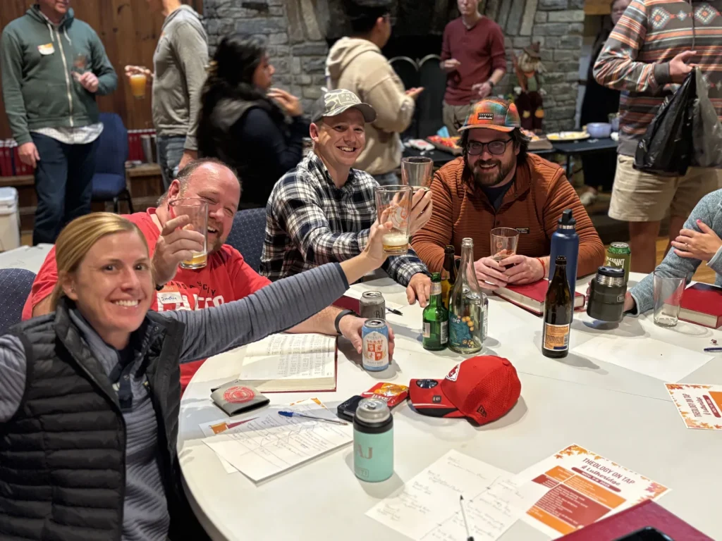 Theology On Tap guests at Lutheridge raising their glasses around a table with Bibles and study sheets