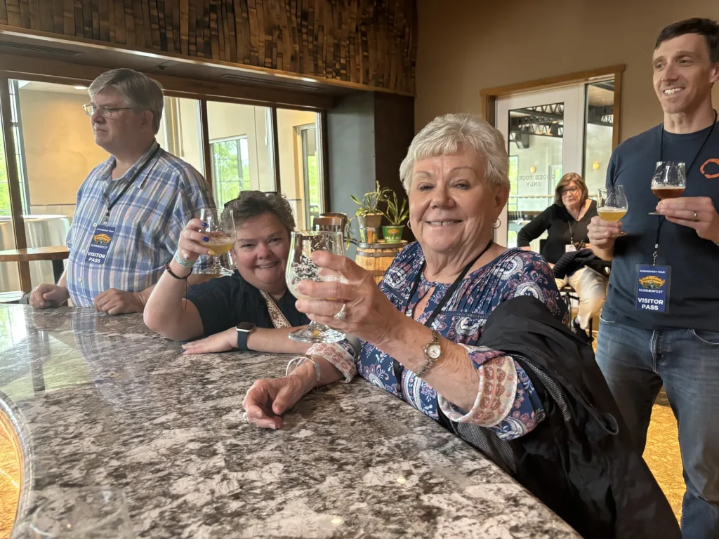 Guests tasting craft beer at a brewery bar, one raising her glass to the camera