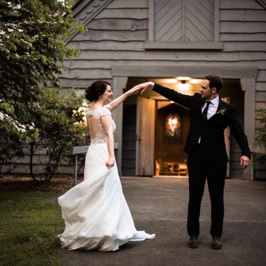 A bride twirls under the groom's raised hand outside the chapel's open door