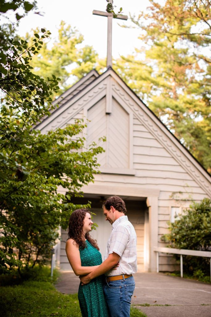 A couple in everyday clothes smile at each other in front of the chapel