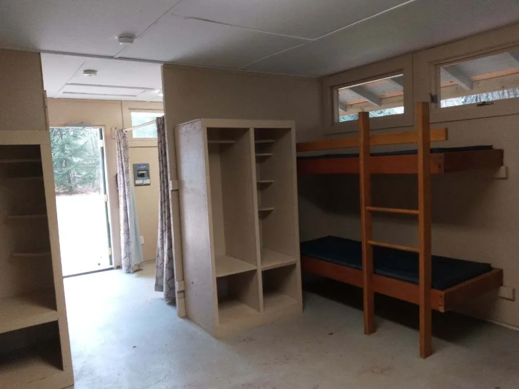 Bunk beds and shelves inside a Wilderness Cabin, the door open to the woods