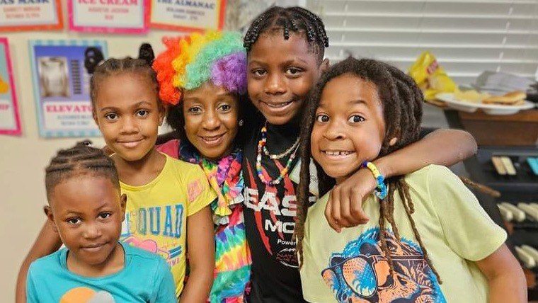 Four campers and a leader in a rainbow wig with their arms around each other at Camp in the City, a Lutheroad day camp in Atlanta