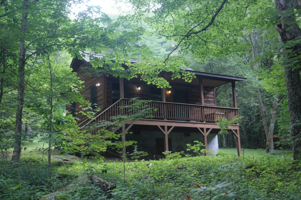 A Cabin Village cabin among the trees, its deck lit at dusk