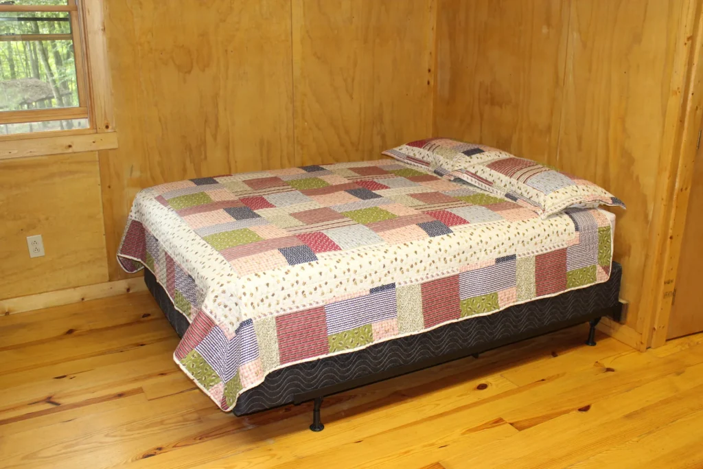 A quilted bed against the pine walls of a Cabin Village cabin