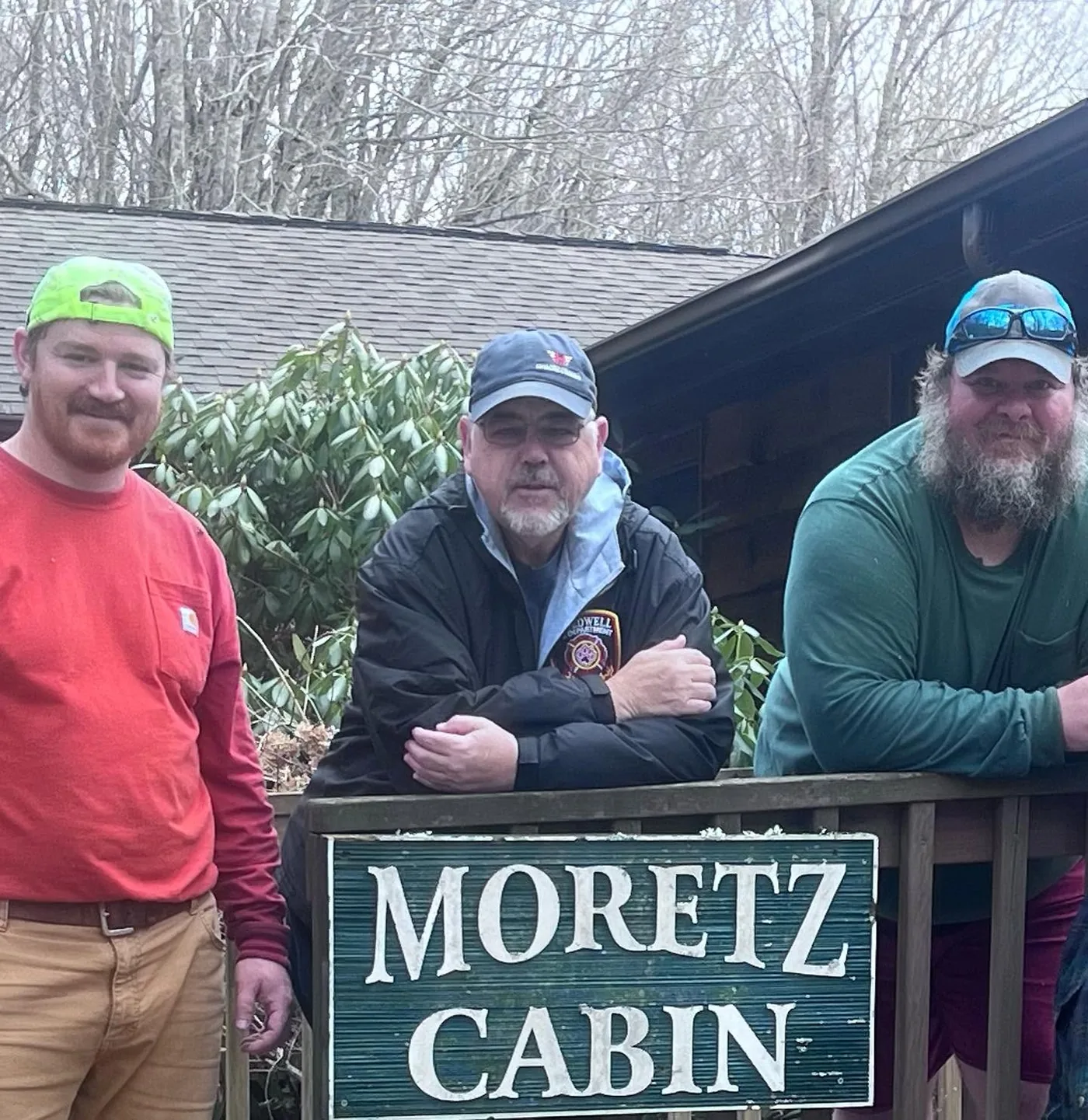 Three volunteers standing behind the Moretz Cabin sign at Lutherock
