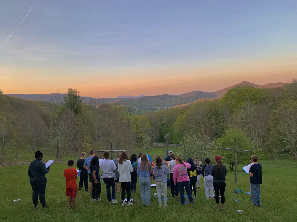 A group gathered for worship on the field at Lutherock at sunset, the mountains behind them