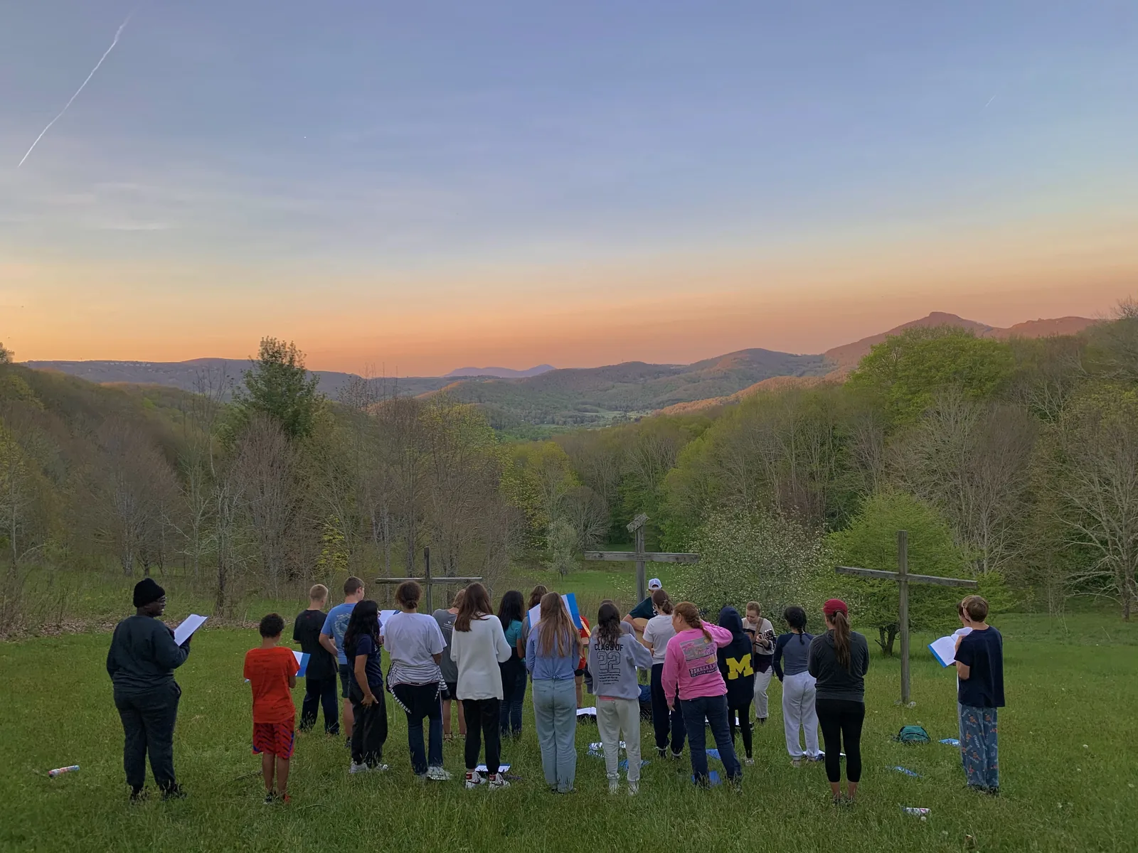A group gathered for worship on the field at Lutherock at sunset, the mountains behind them