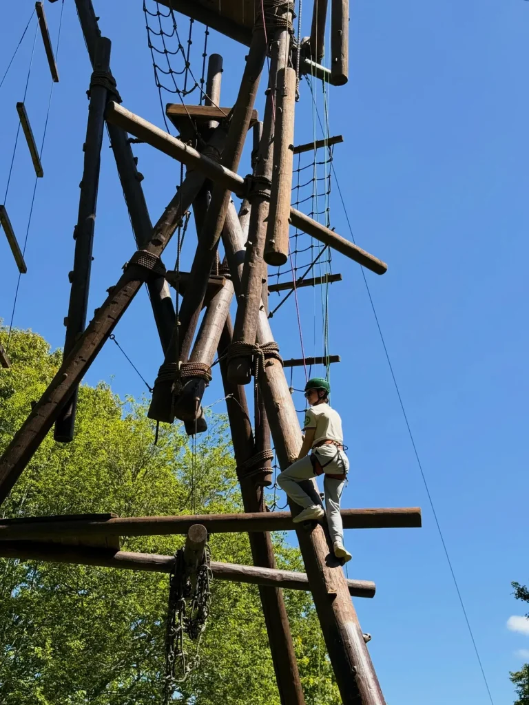 A climber in a helmet and harness partway up a wooden climbing tower.
