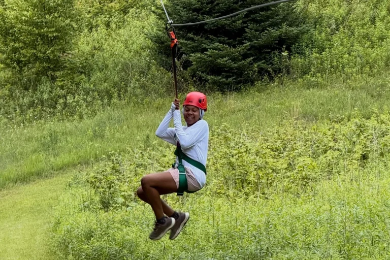 A camper in a red helmet riding the zip line across the field at Lutherock