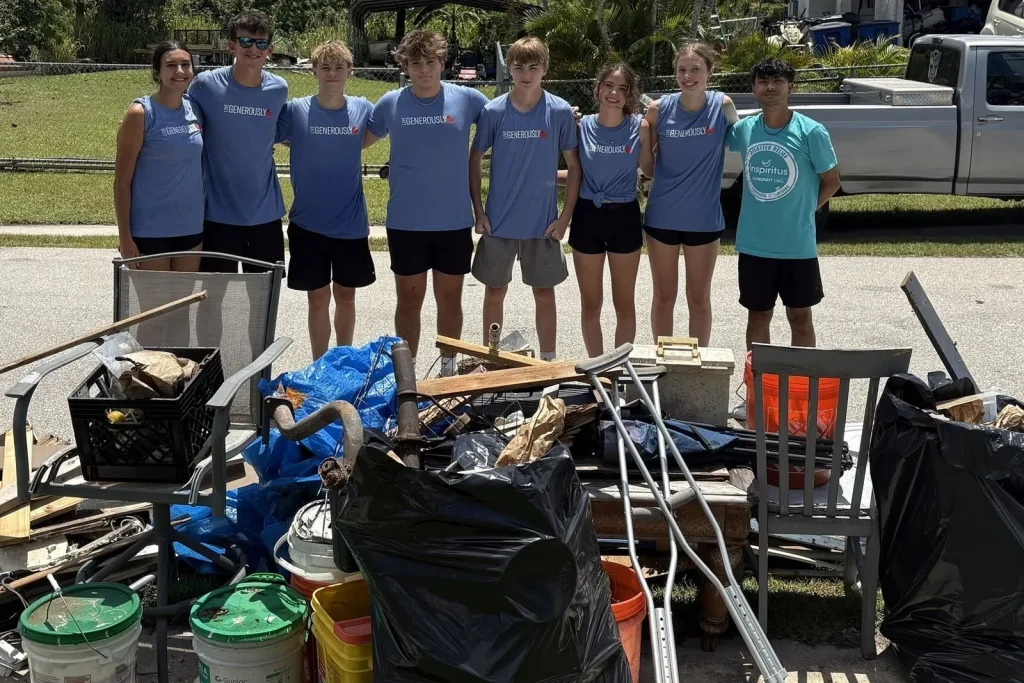 A youth service team in matching shirts standing behind a pile of storm debris they cleared