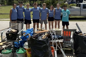 A youth service team in matching shirts standing behind a pile of storm debris they cleared