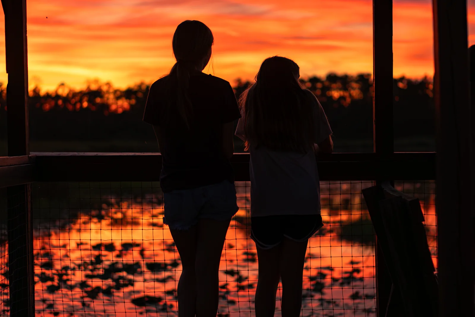 Two campers silhouetted on the covered dock against a blazing orange sky over the lake at Luther Springs