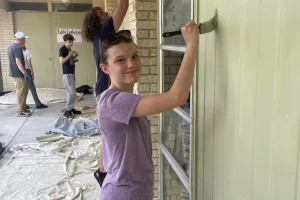 A camper painting the trim of a church building on a Luther Springs servant camp service project