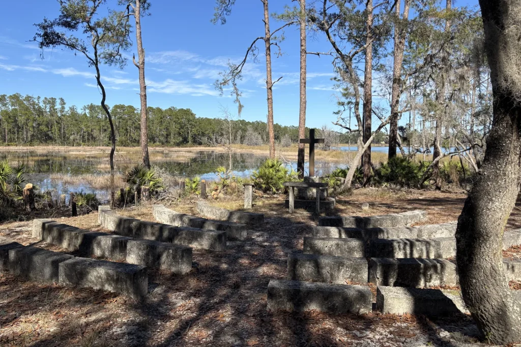 Rows of stone benches facing the cross at the outdoor chapel at Luther Springs, the marsh and pines beyond
