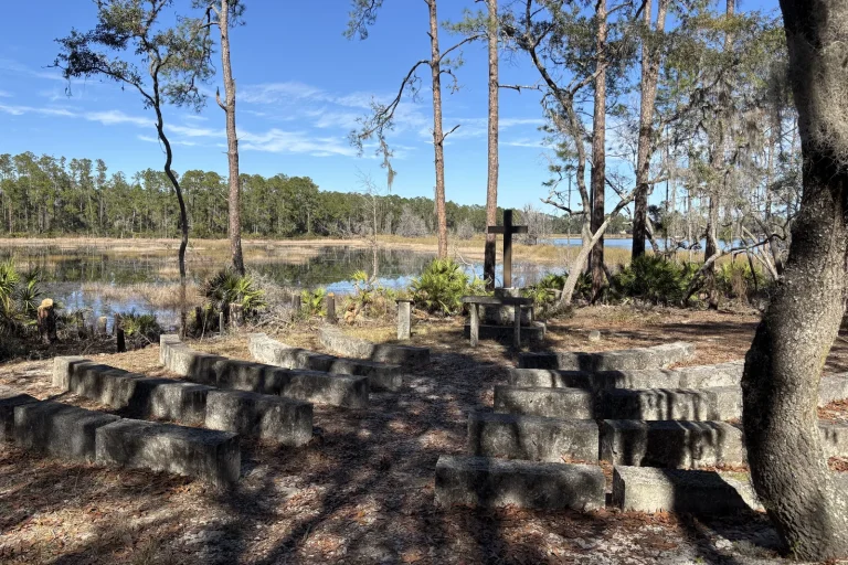 Rows of stone benches facing the cross at the outdoor chapel at Luther Springs, the marsh and pines beyond