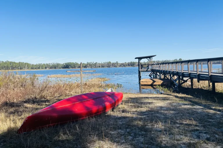 A red canoe pulled up on the shore beside the covered dock on the lake at Luther Springs, under a clear blue sky