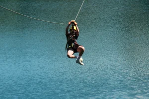 A camper riding a zip line high above clear blue-green water